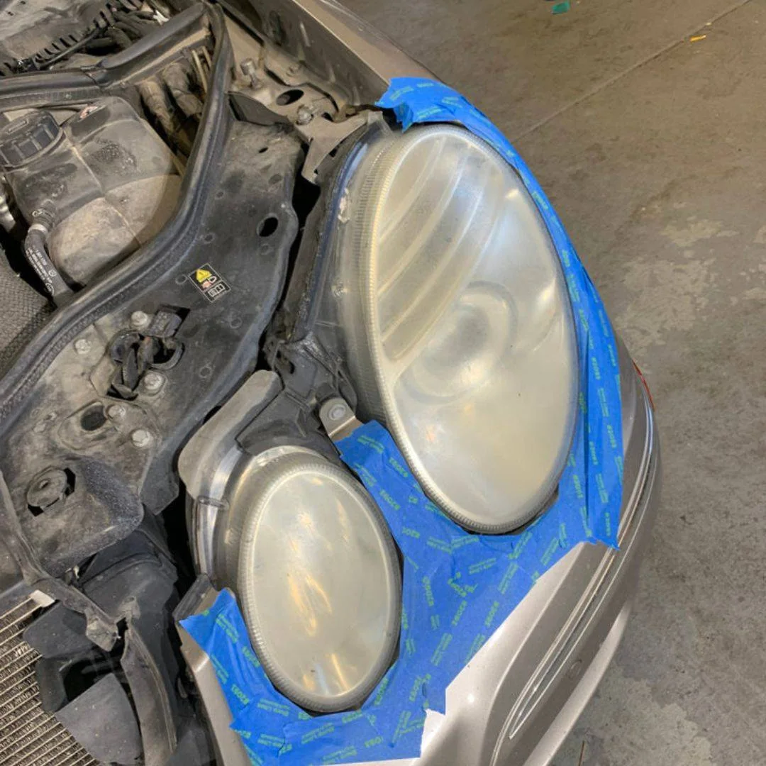 A cloudy, yellowed Mercedes headlight, taped off before restoration
