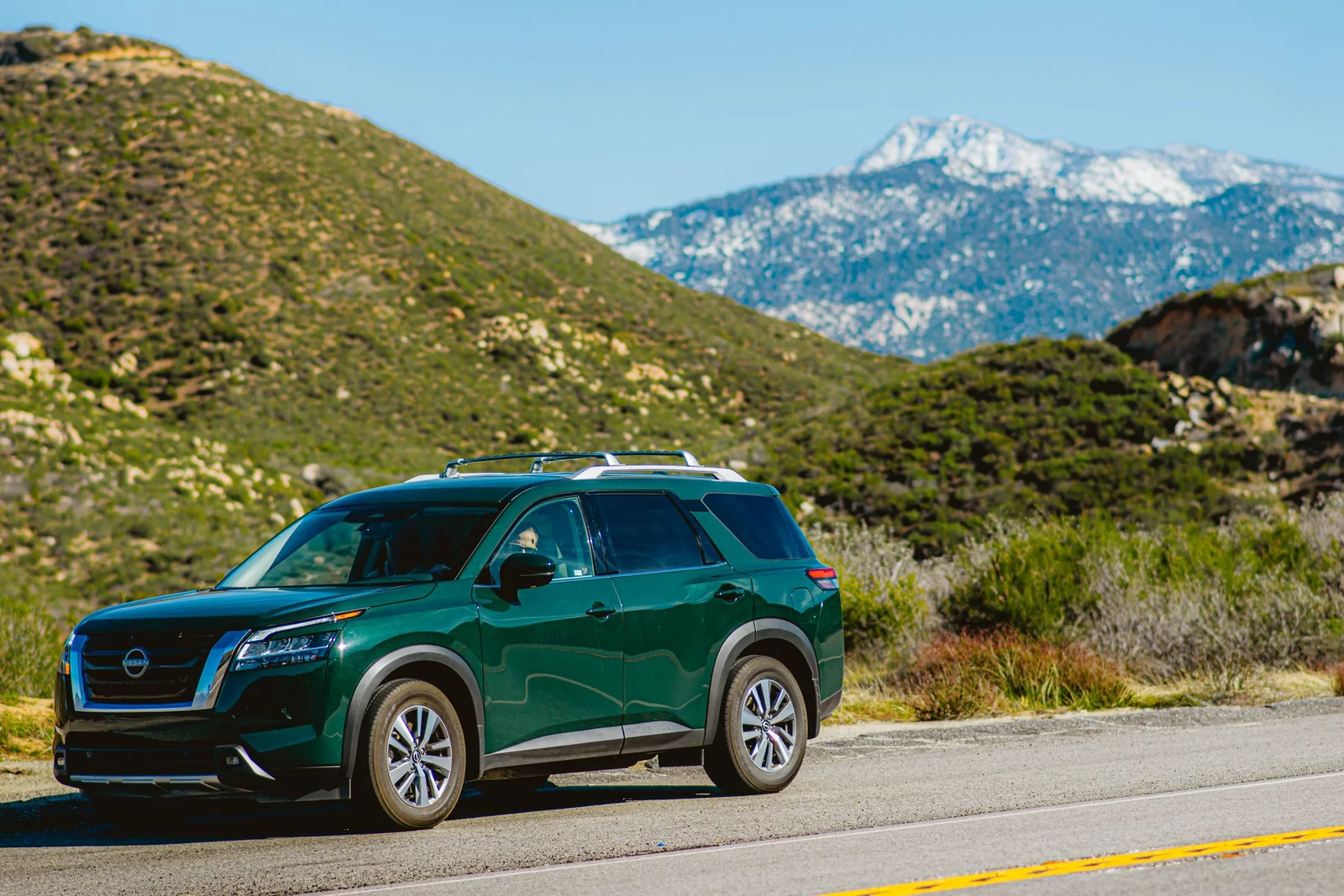A green SUV out in strong sun on a mountain road