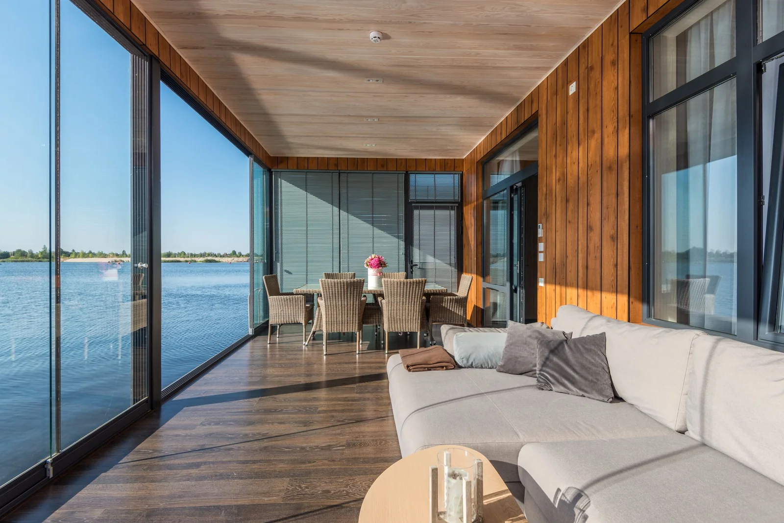A glass-walled sunroom with a sofa and a view over the water