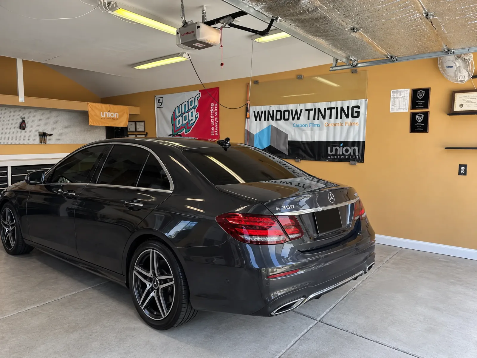 A dark Mercedes with tinted windows in the Asap Window Tint bay, Union Window Films banners on the wall