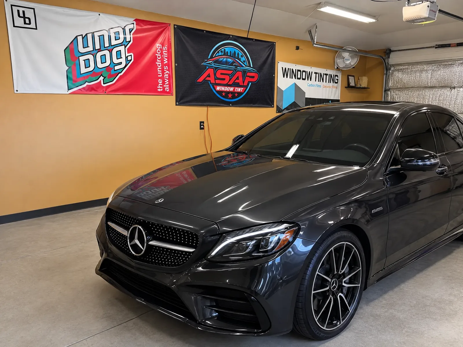The Asap Window Tint bay with their banner on the wall and a dark tinted Mercedes